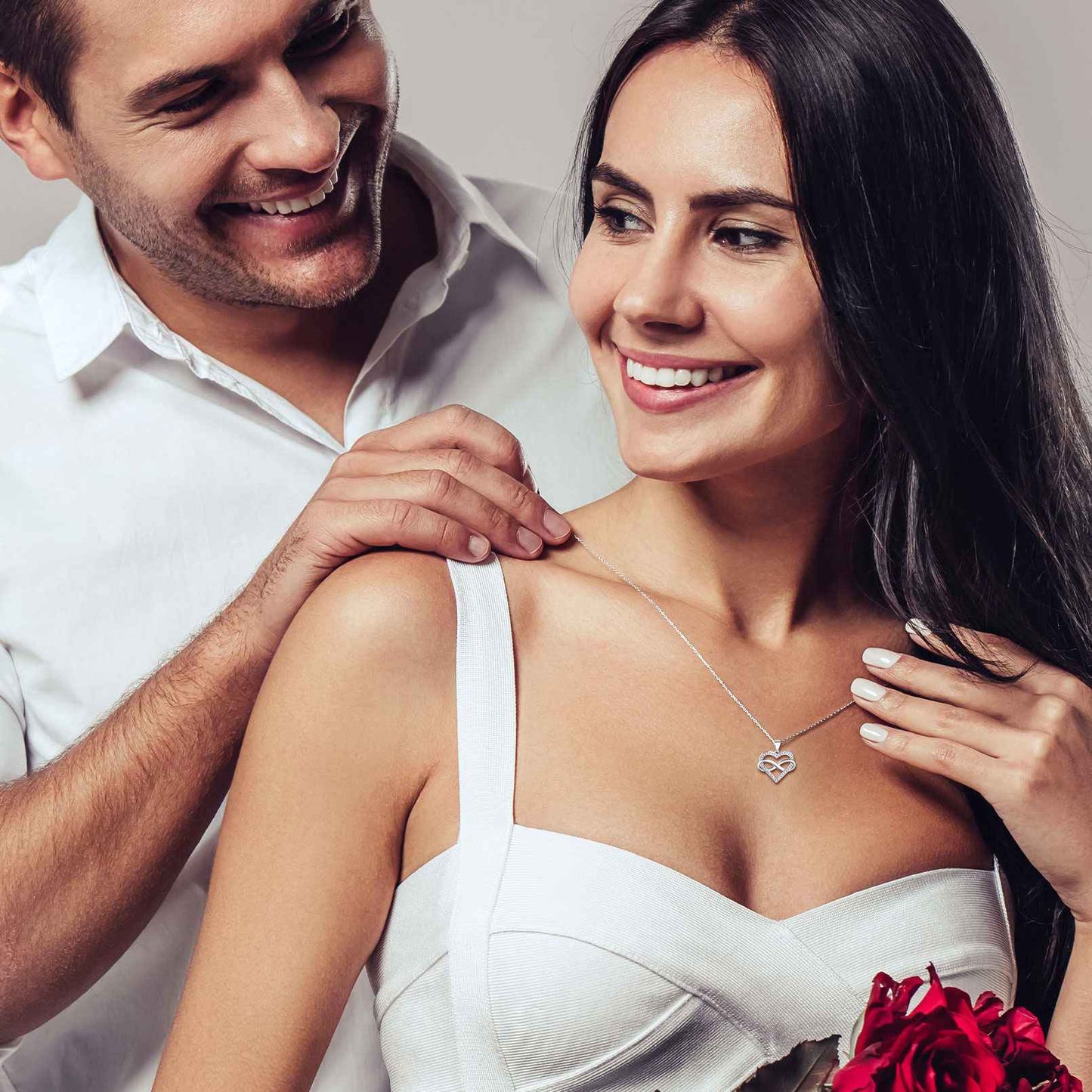 Man adjusting a infinity heart necklace on a woman, both smilin