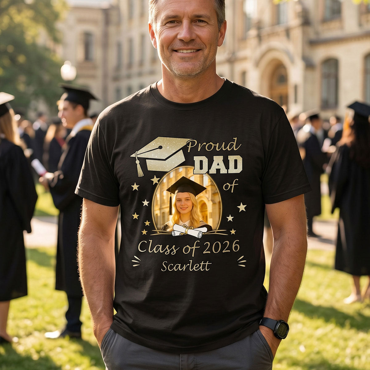 Man wearing a black custom graduation t-shirt with 'Proud Dad of Class of 2026' design, standing outdoors with graduation ceremony background.