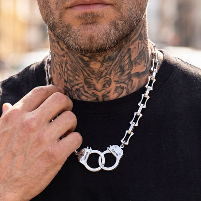 Man wearing a black shirt with a silver handcuff necklace, close-up on neck and hand.