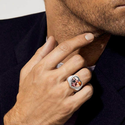 Man wearing a heart photo ring with a photo on it, touching his chin.