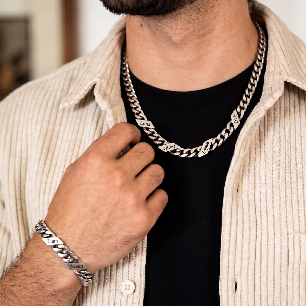 Man wearing a silver chain necklace and bracelet with engraved names.