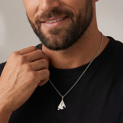 Man wearing a silver puzzle necklace with a unique pendant against a neutral background