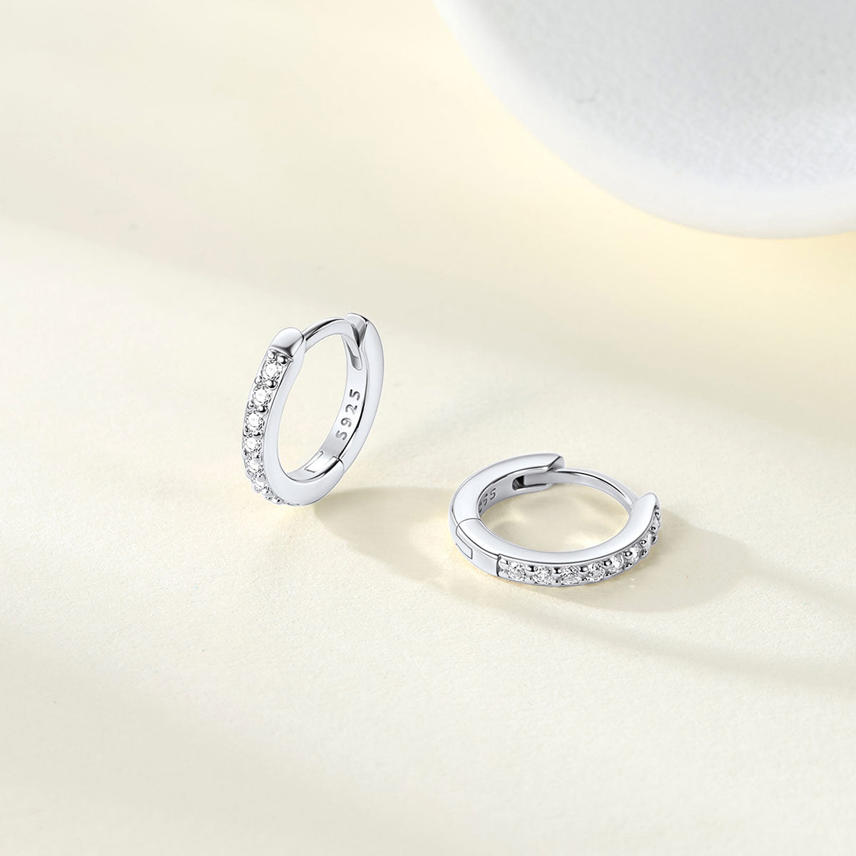 Pair of silver cubic zirconia huggie earrings with embedded stones on a light beige background
