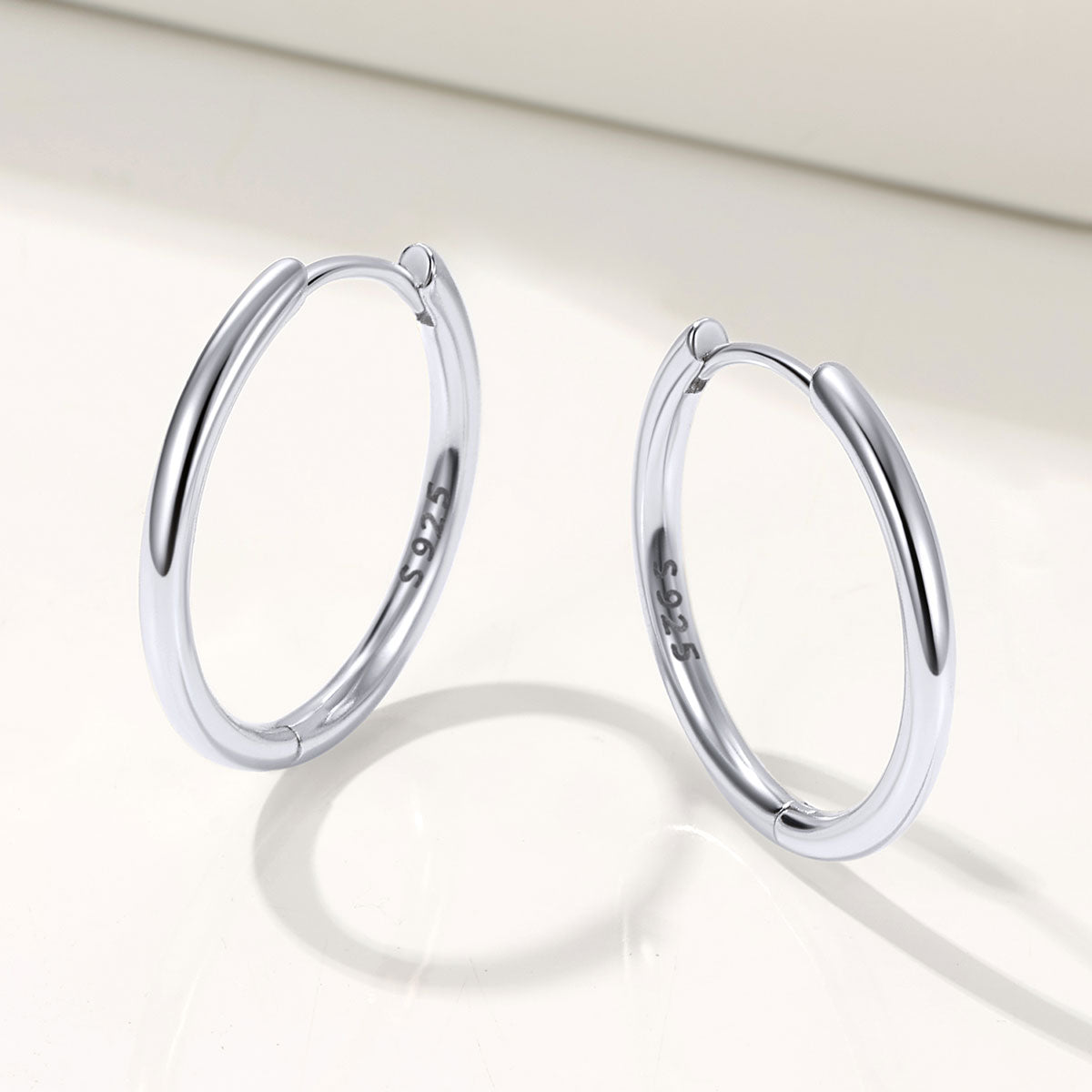 Pair of silver huggie earrings on a light background