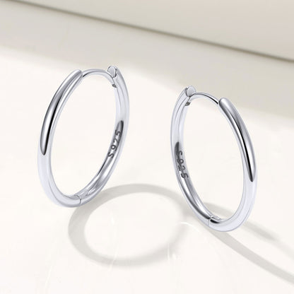 Pair of silver huggie earrings on a light background