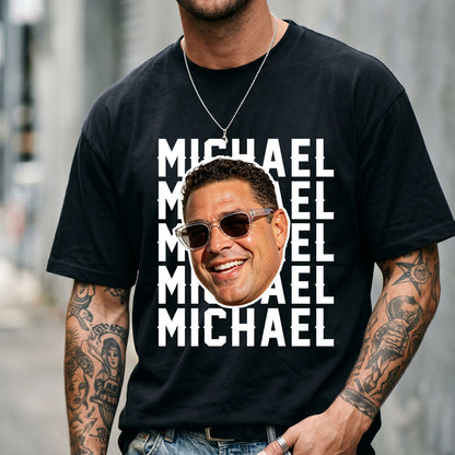 Person wearing a black face t-shirt with a graphic of a smiling man and the name 'Michael' repeated.
