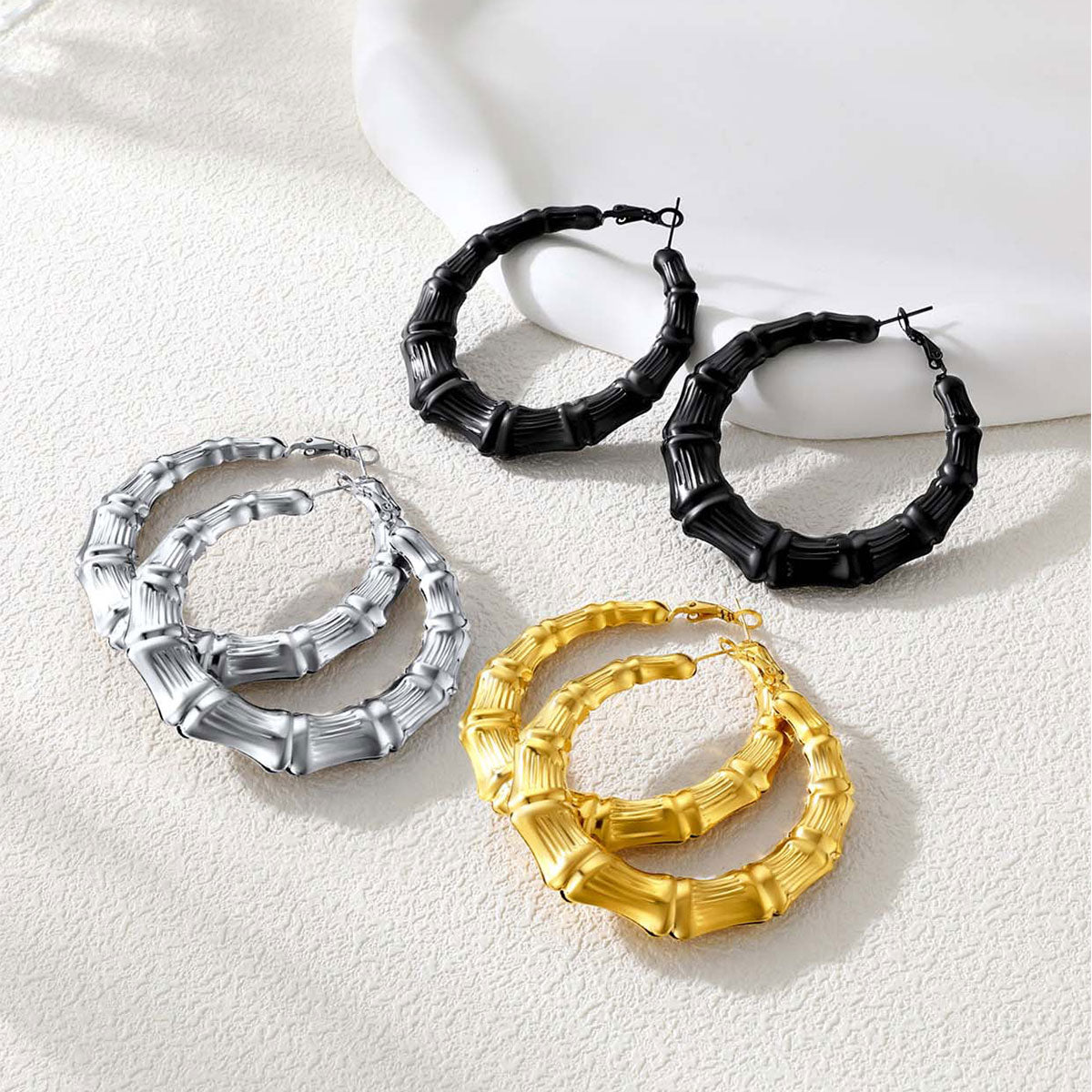 Set of bamboo hoop earrings in black, gold, and silver on a light background