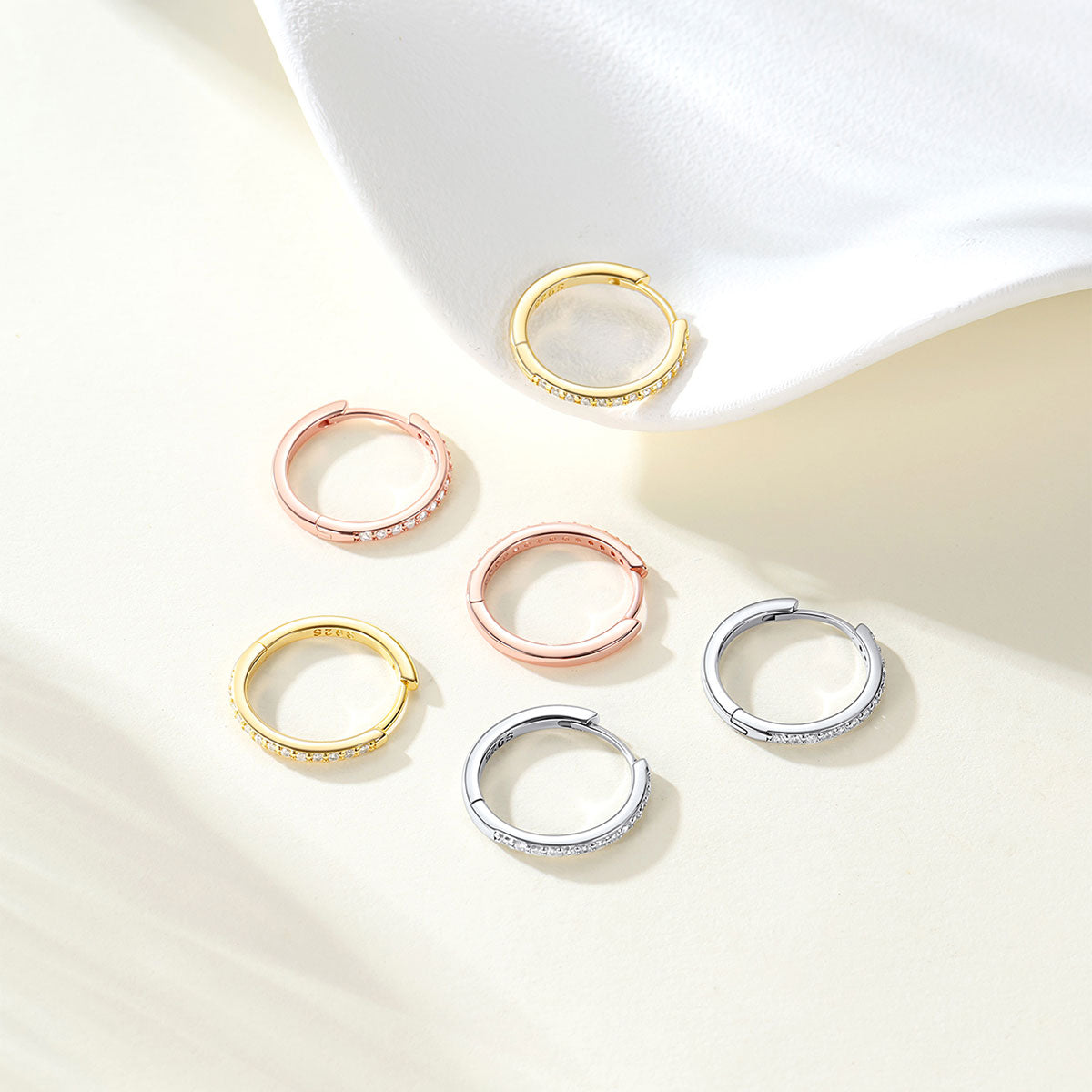 Set of gold, rose gold, and silver huggie earrings on a light background
