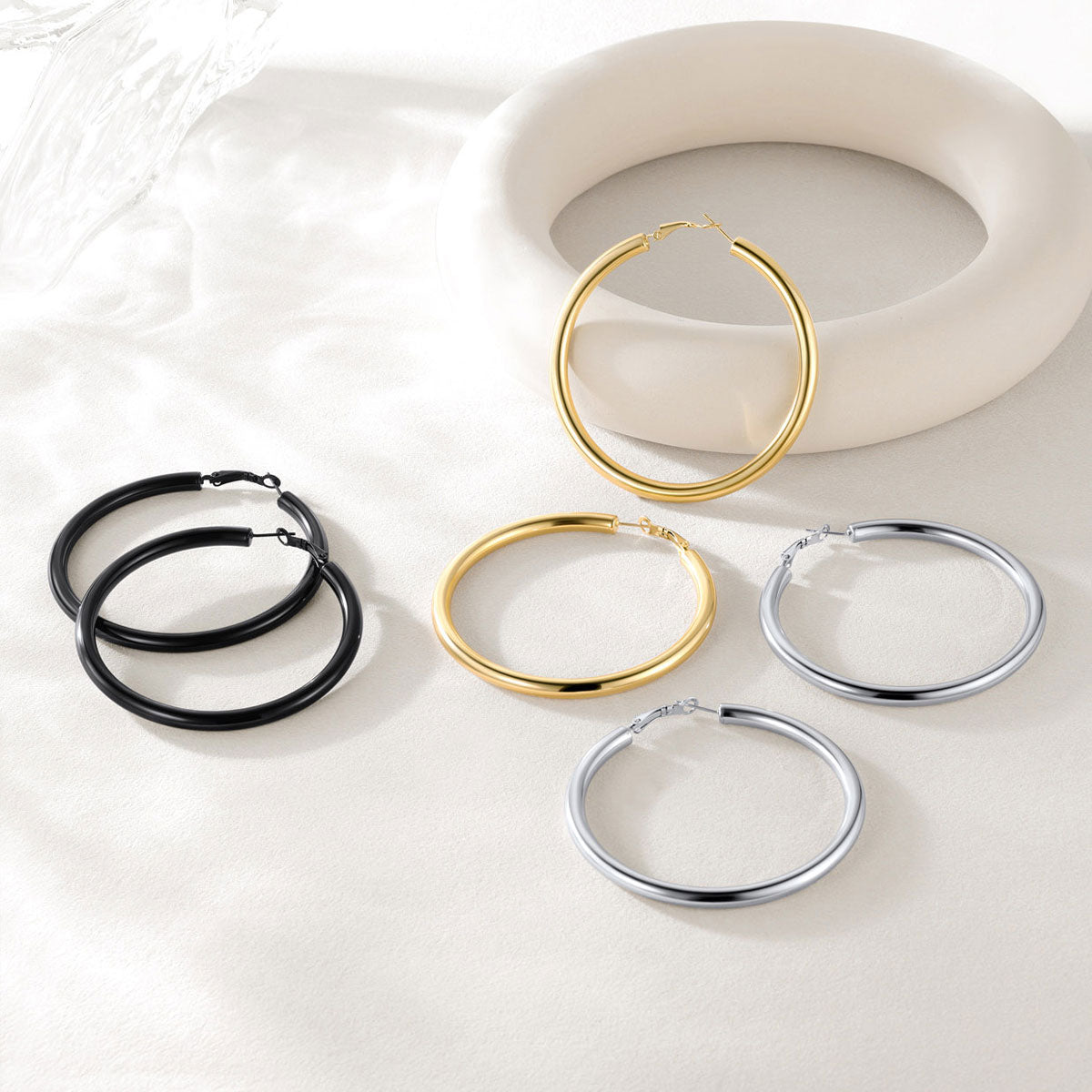 Set of hoop earrings in gold, black, and silver on a light background