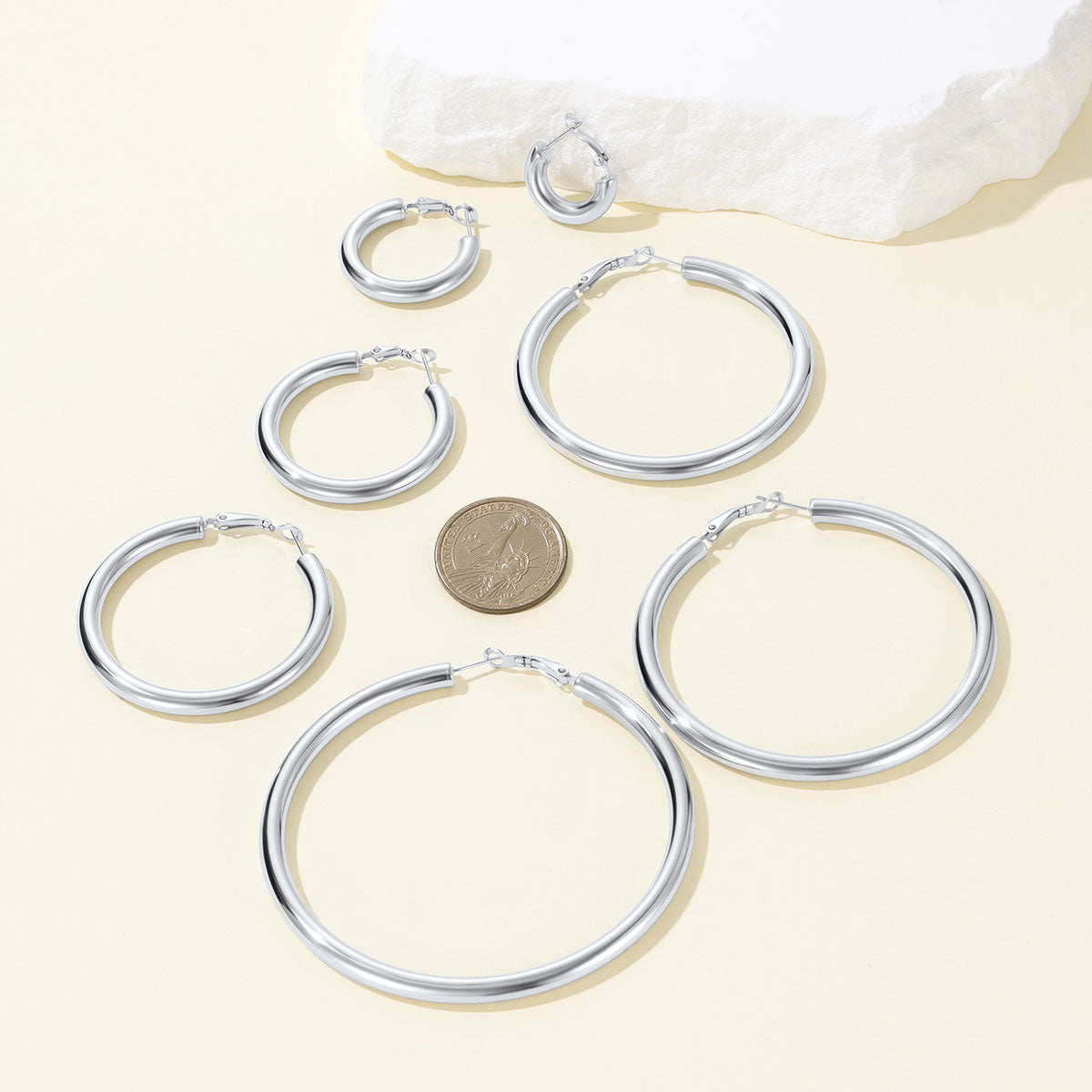 Set of silver hoop earrings with a coin for size reference on a light background