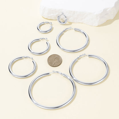 Set of silver hoop earrings with a coin for size reference on a light background