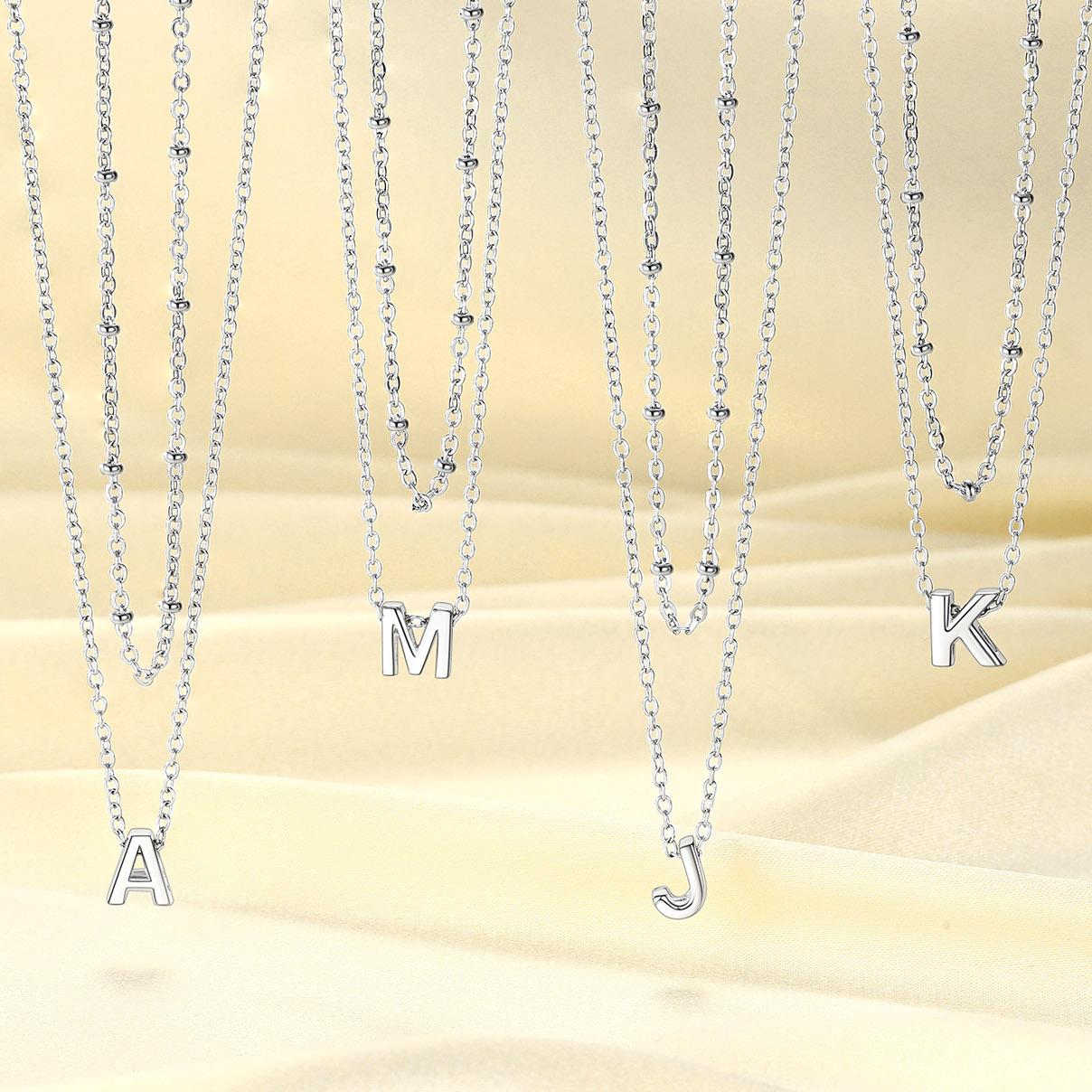 Set of silver initial necklaces with letter pendants on a beige background