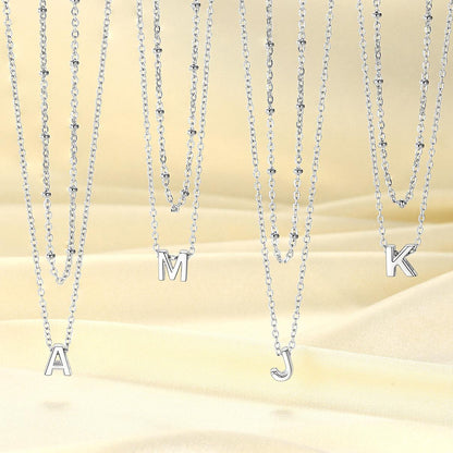 Set of silver initial necklaces with letter pendants on a beige background