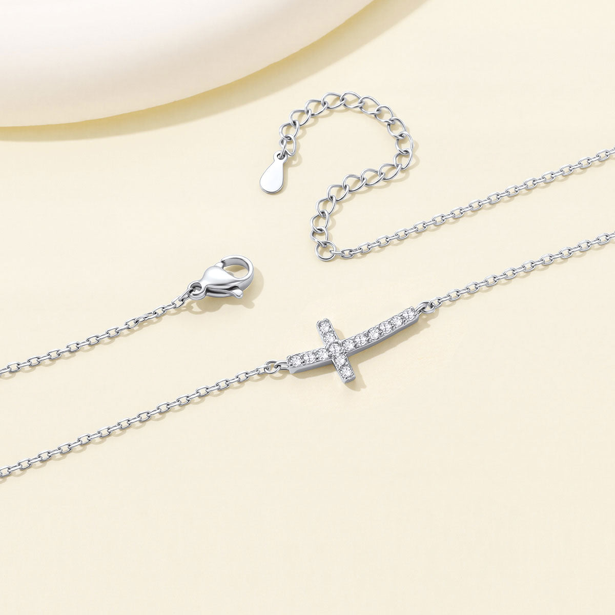 Silver Dainty Cubic Zirconia Sideways Cross Necklace for Women on a light yellow background