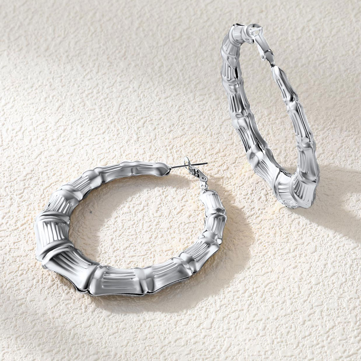 Silver bamboo hoop earrings on a textured beige surface