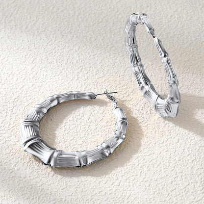 Silver bamboo hoop earrings on a textured beige surface