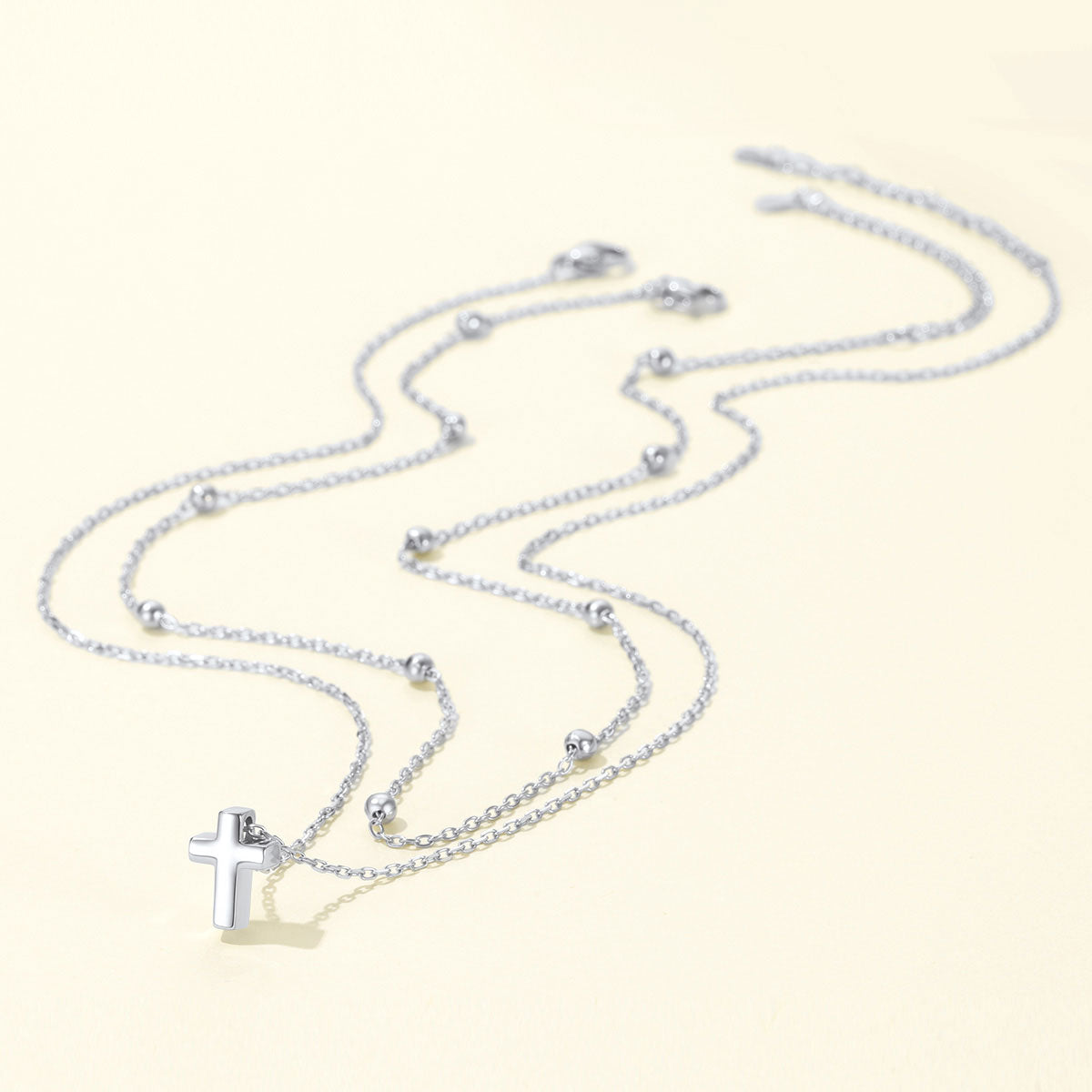 Silver cross necklace with a cross pendant on a light beige background