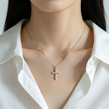 Silver cross necklace worn by a person in a white shirt