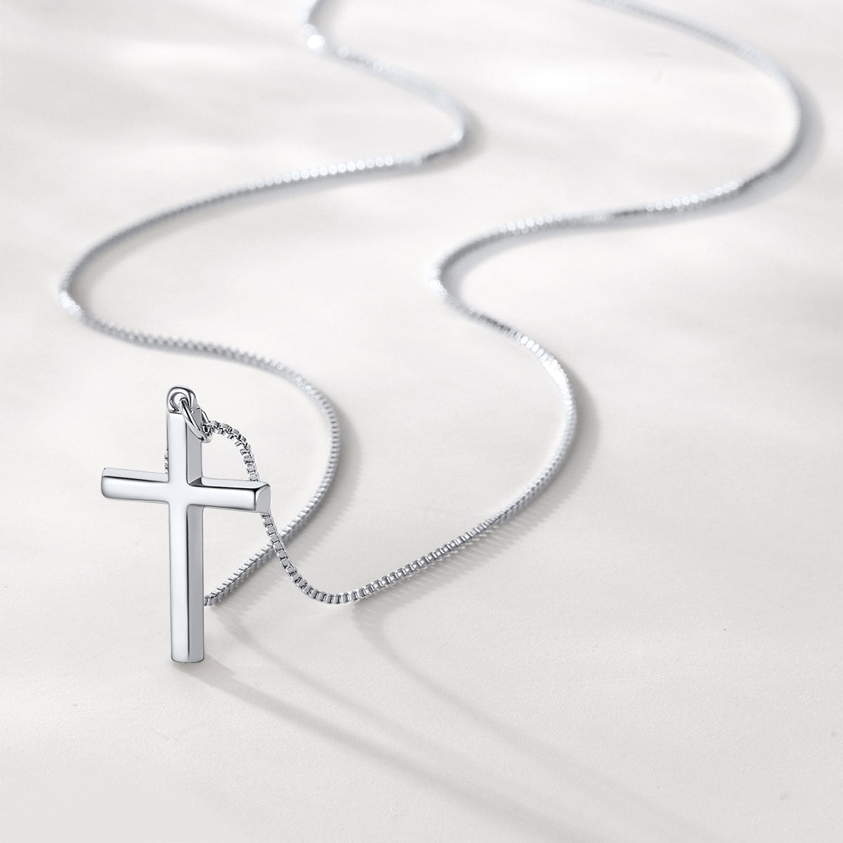 Silver cross pendant on a chain against a white background