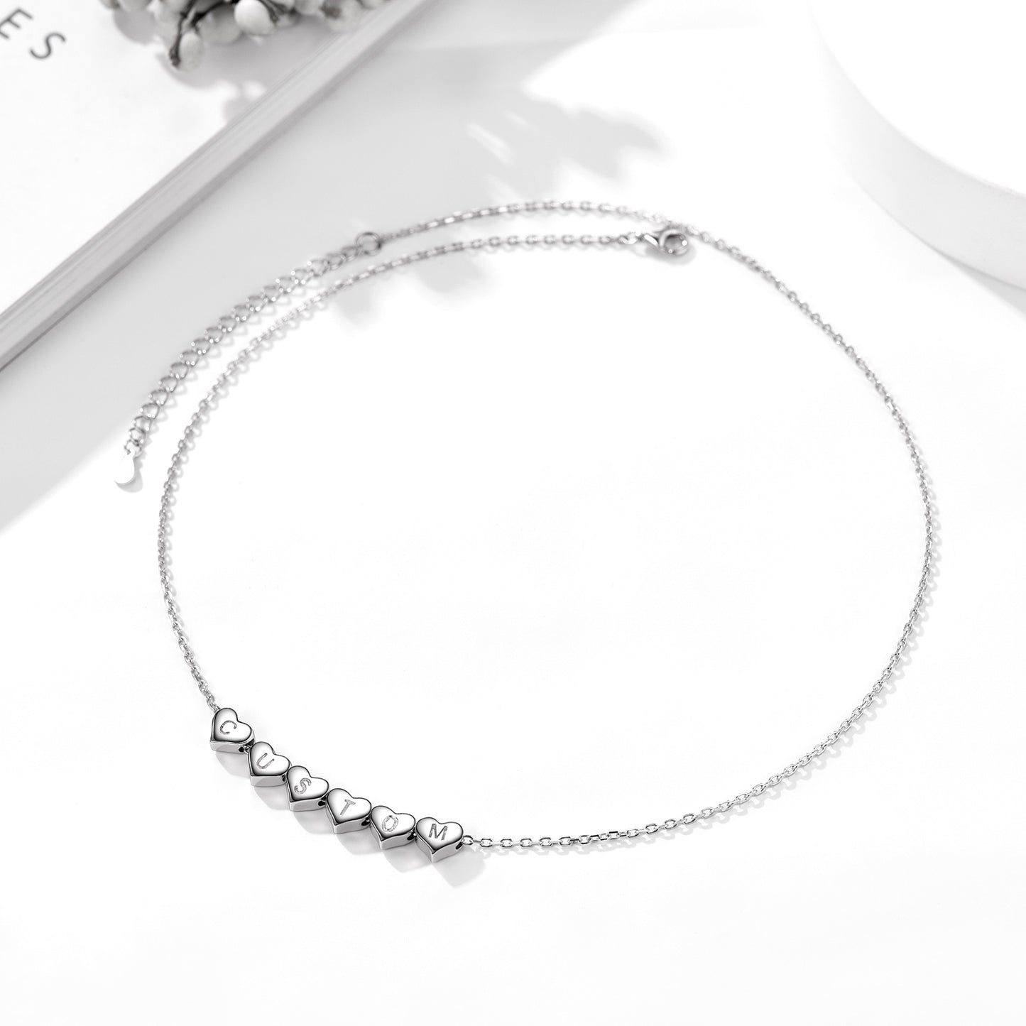 Silver heart charm initial necklace with heart-shaped pendants on a white background
