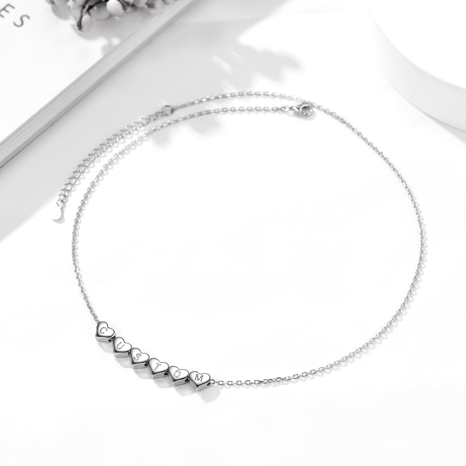 Silver heart charm initial necklace with heart-shaped pendants on a white background