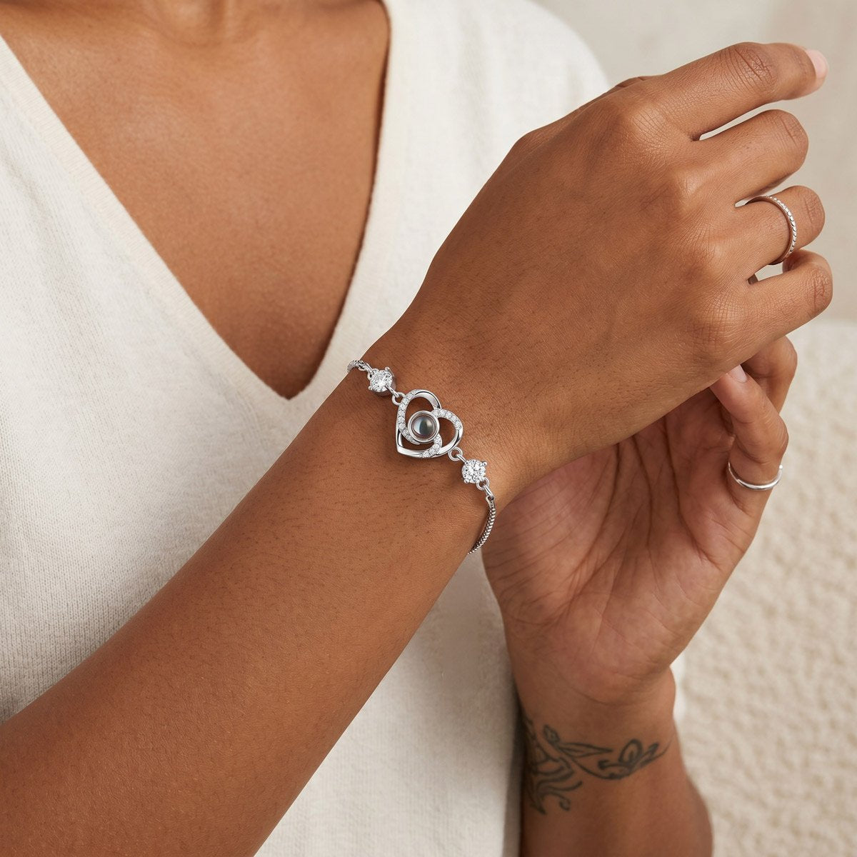 Silver heart charm projection bracelet on a wrist with a neutral background