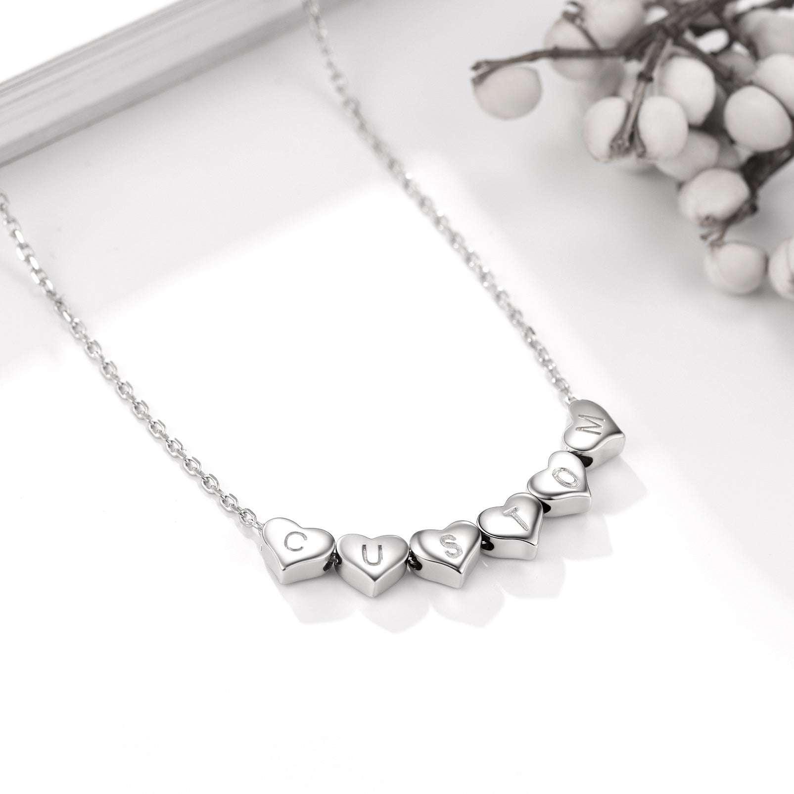 Silver heart initial necklace with heart-shaped pendants on a white surface