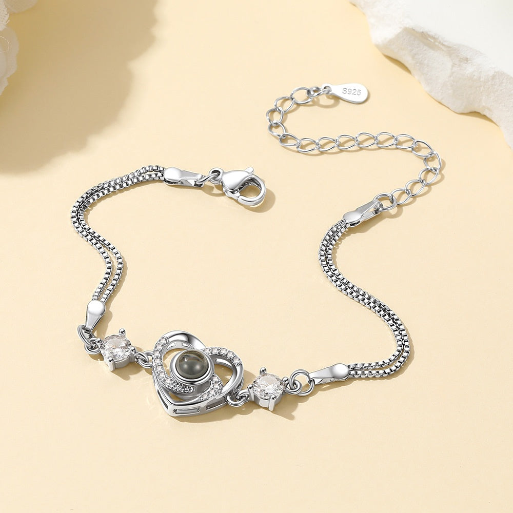 Silver heart projection bracelet with heart-shaped clasp and gemstone on a beige background
