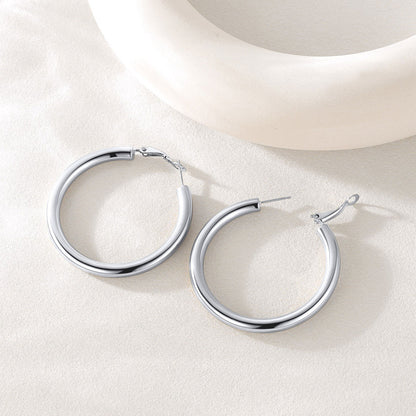 Silver hoop earrings on a light beige surface with a neutral background