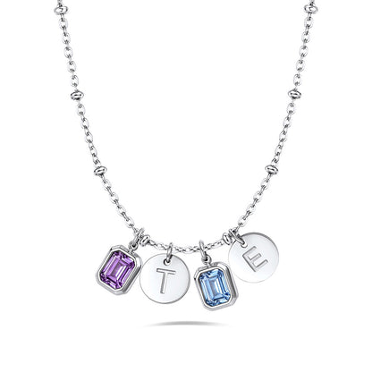 A silver initial birthstone necklace featuring two round silver discs engraved with the letters T, O, and L, alongside two rectangular gemstone charms in purple and light blue, suspended from a silver beaded chain on a white background.