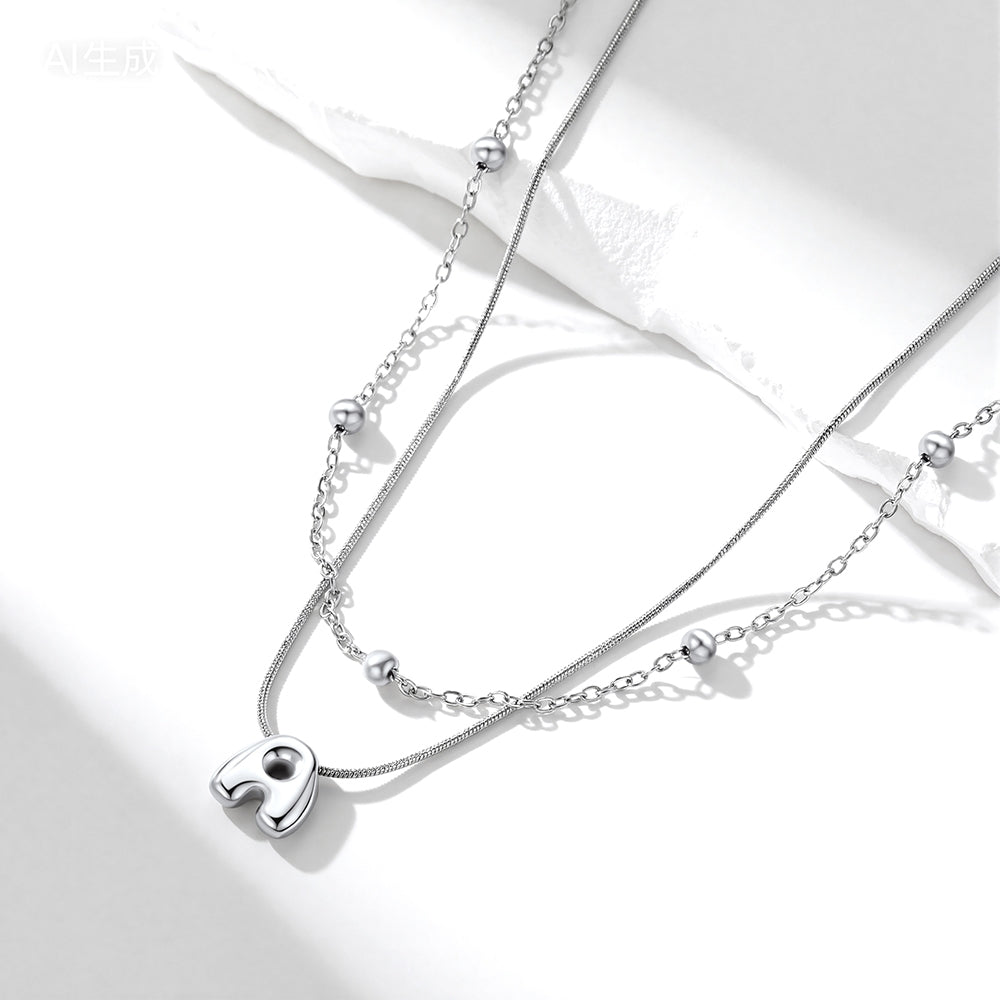 Silver initial layered necklace with a heart pendant on a white background