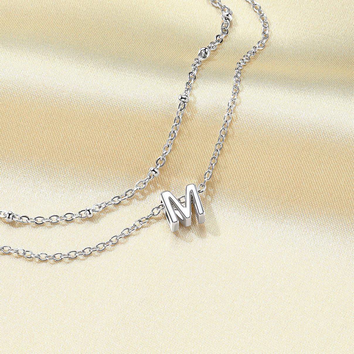 Silver initial necklace with a 'M' pendant on a beige fabric background