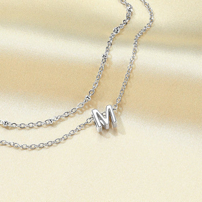 Silver initial necklace with a 'M' pendant on a beige fabric background