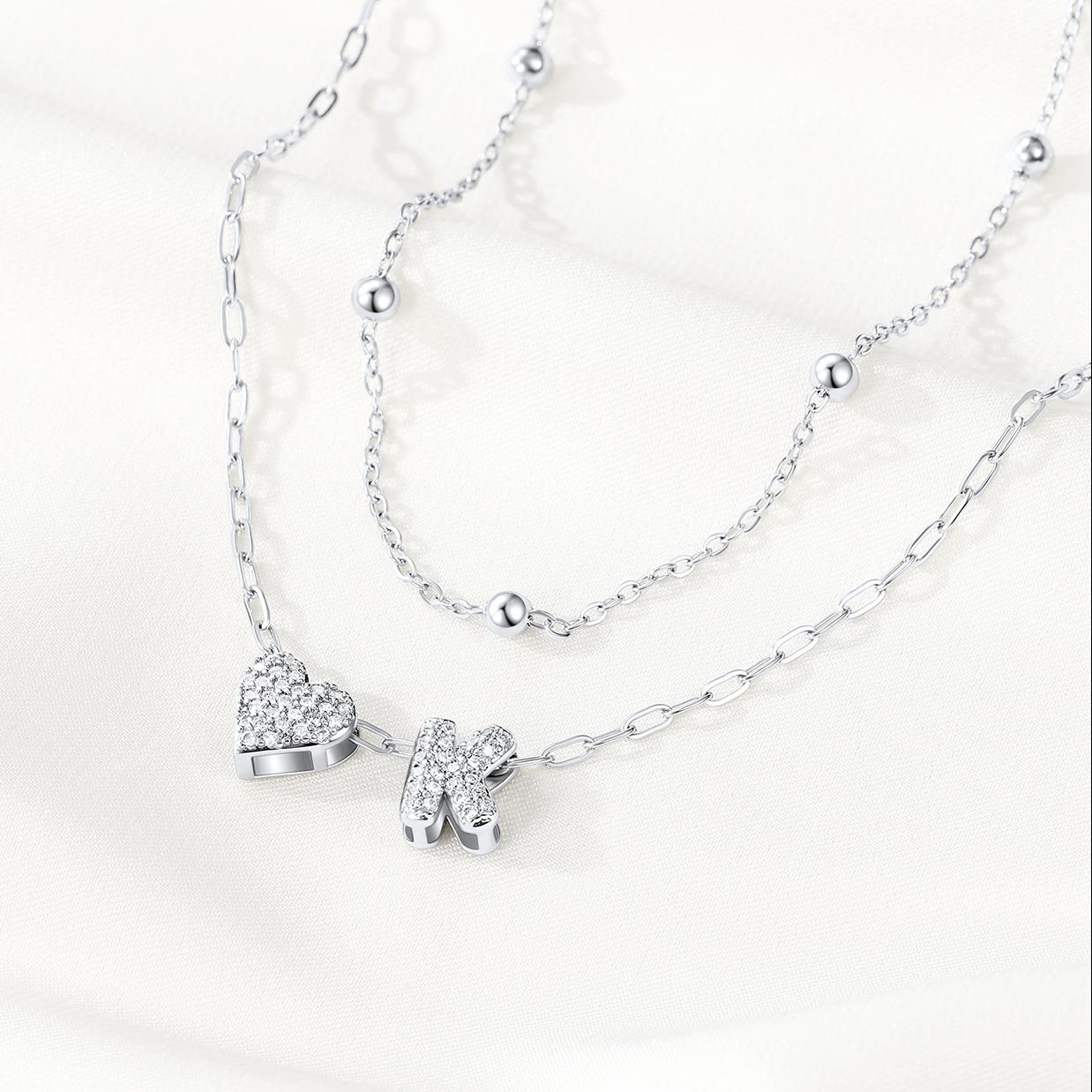 Silver initial necklace with heart and shoe pendants on a white background