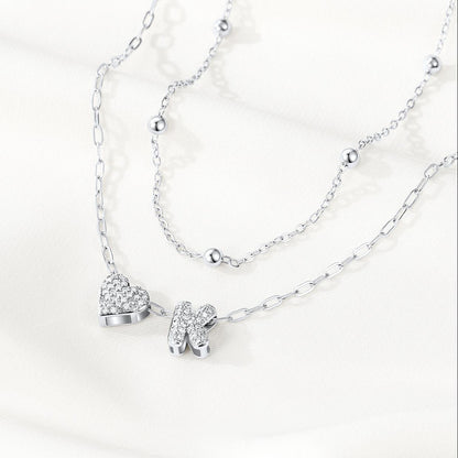Silver initial necklace with heart and shoe pendants on a white background