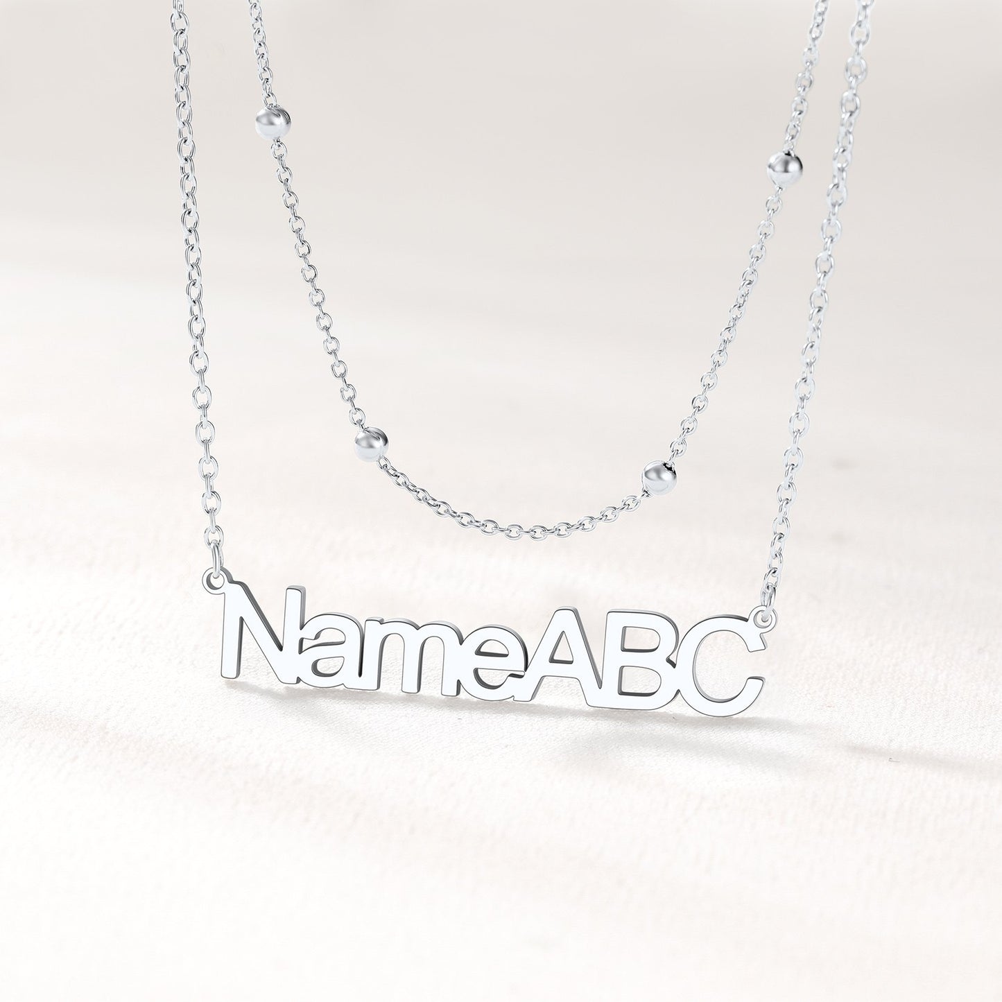 Silver layered name necklace on a light gray background