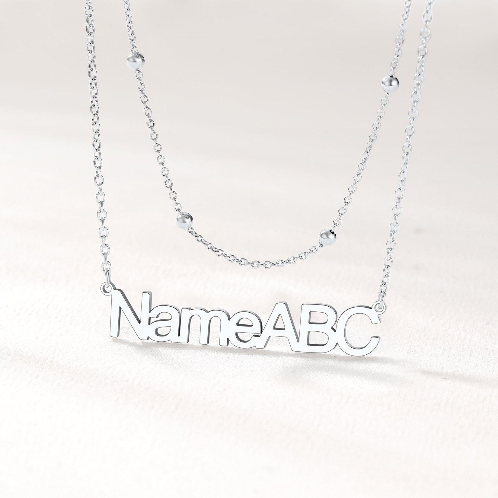 Silver layered name necklace on a light gray background