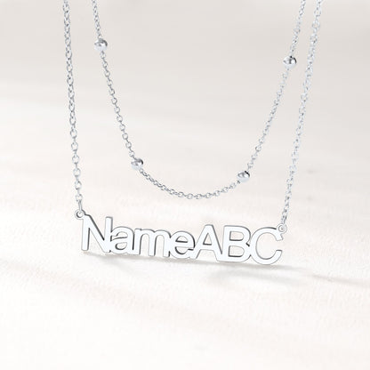 Silver layered name necklace on a light gray background