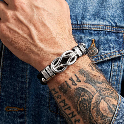 Silver multi name leather bracelet with intricate design worn on a wrist with tattoos, against a denim background.