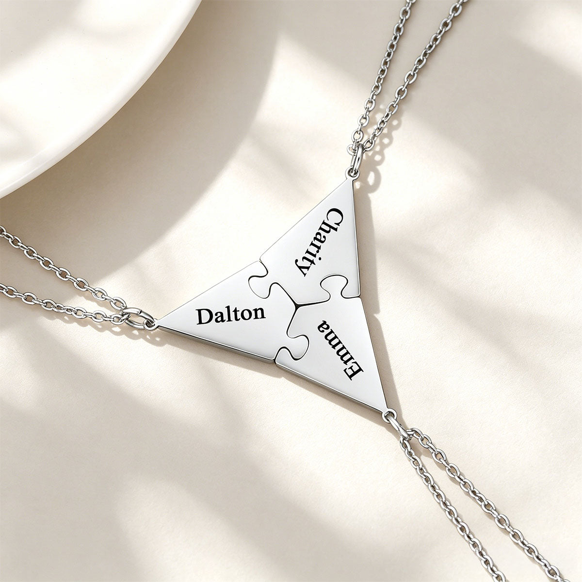 Silver puzzle matching necklace with engraved names on a beige background