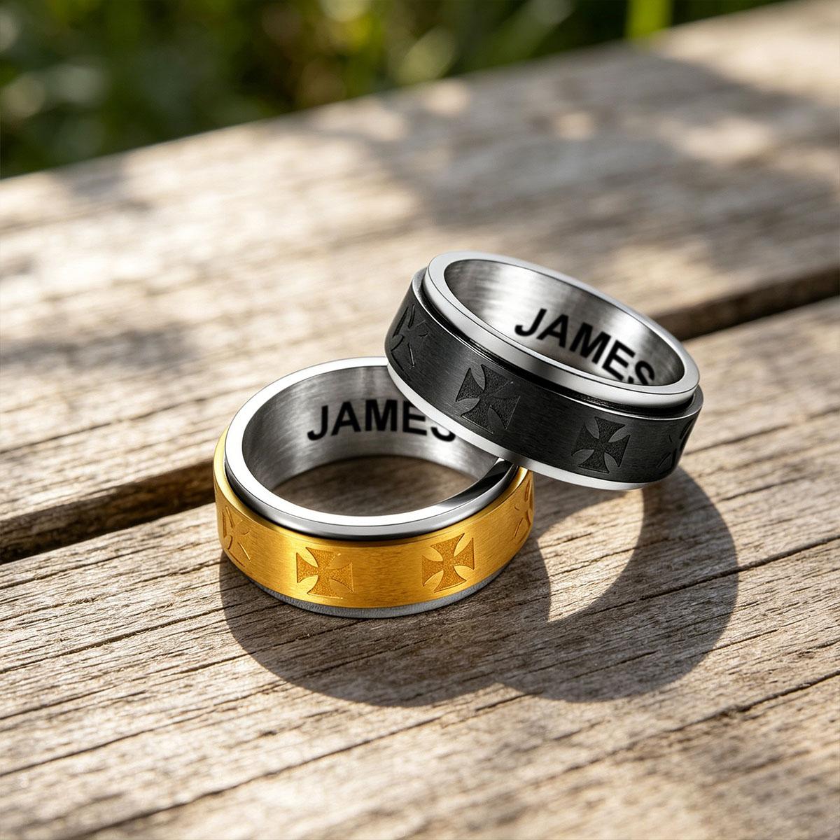 Three Knights Templar rings in gold, silver, and black on a wooden surface with 'JAMES' engraved.