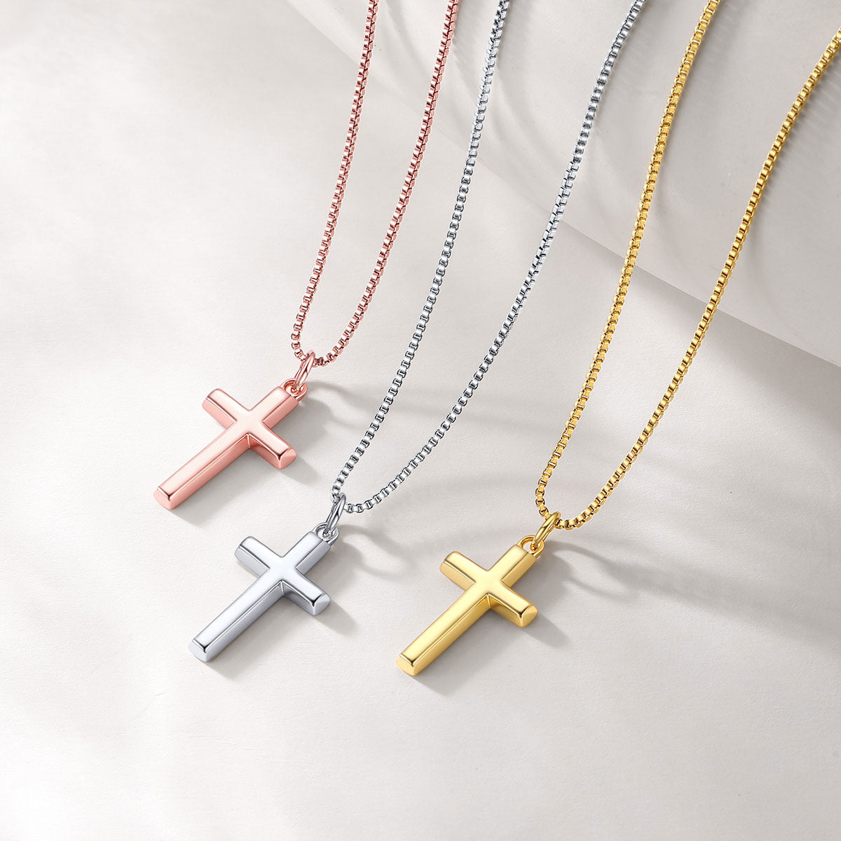 Three cross necklaces in gold, silver, and rose gold on a light background
