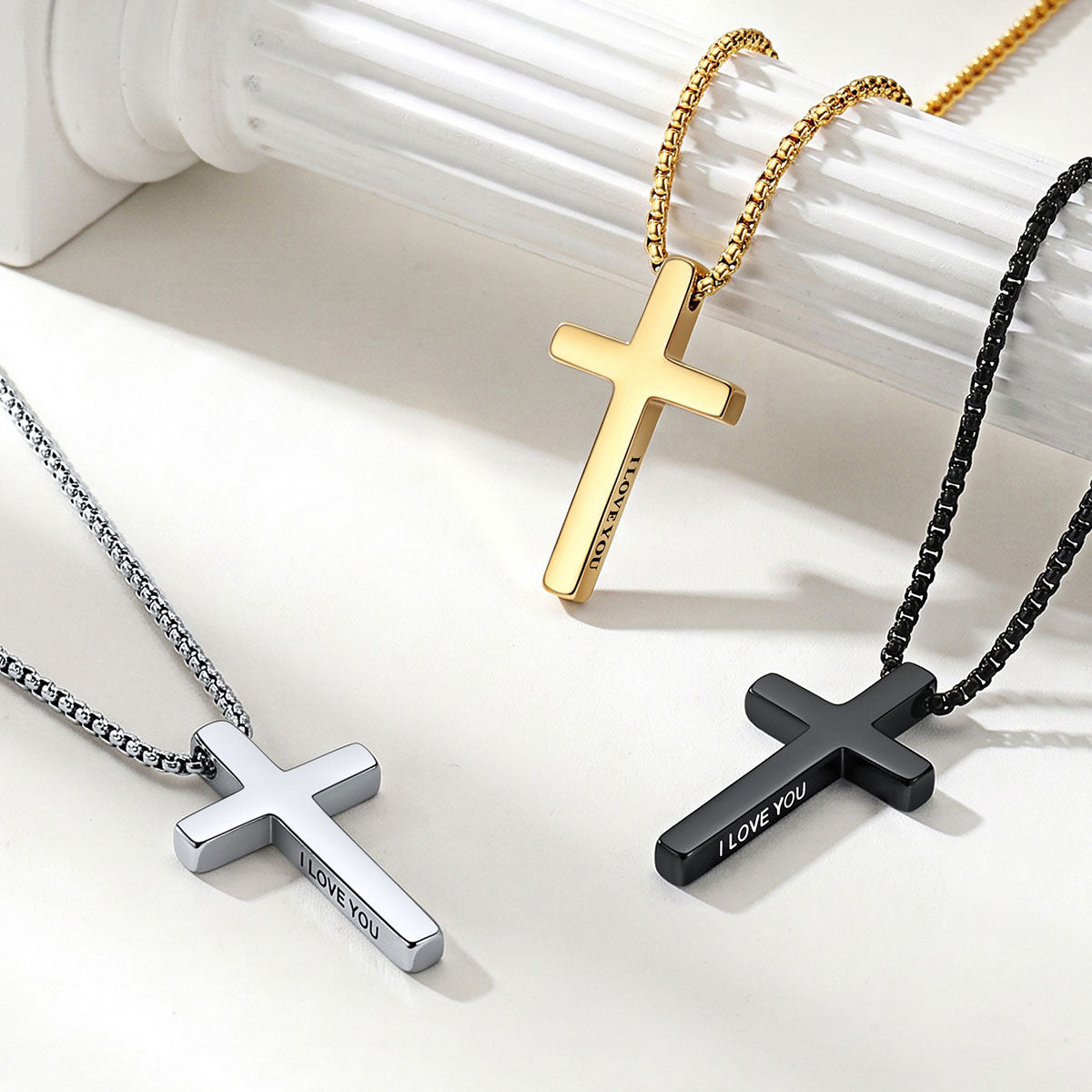 Three engraved cross necklaces in gold, silver, and black on a white background