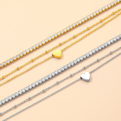 Three gold and silver heart-shaped anklets on a beige background