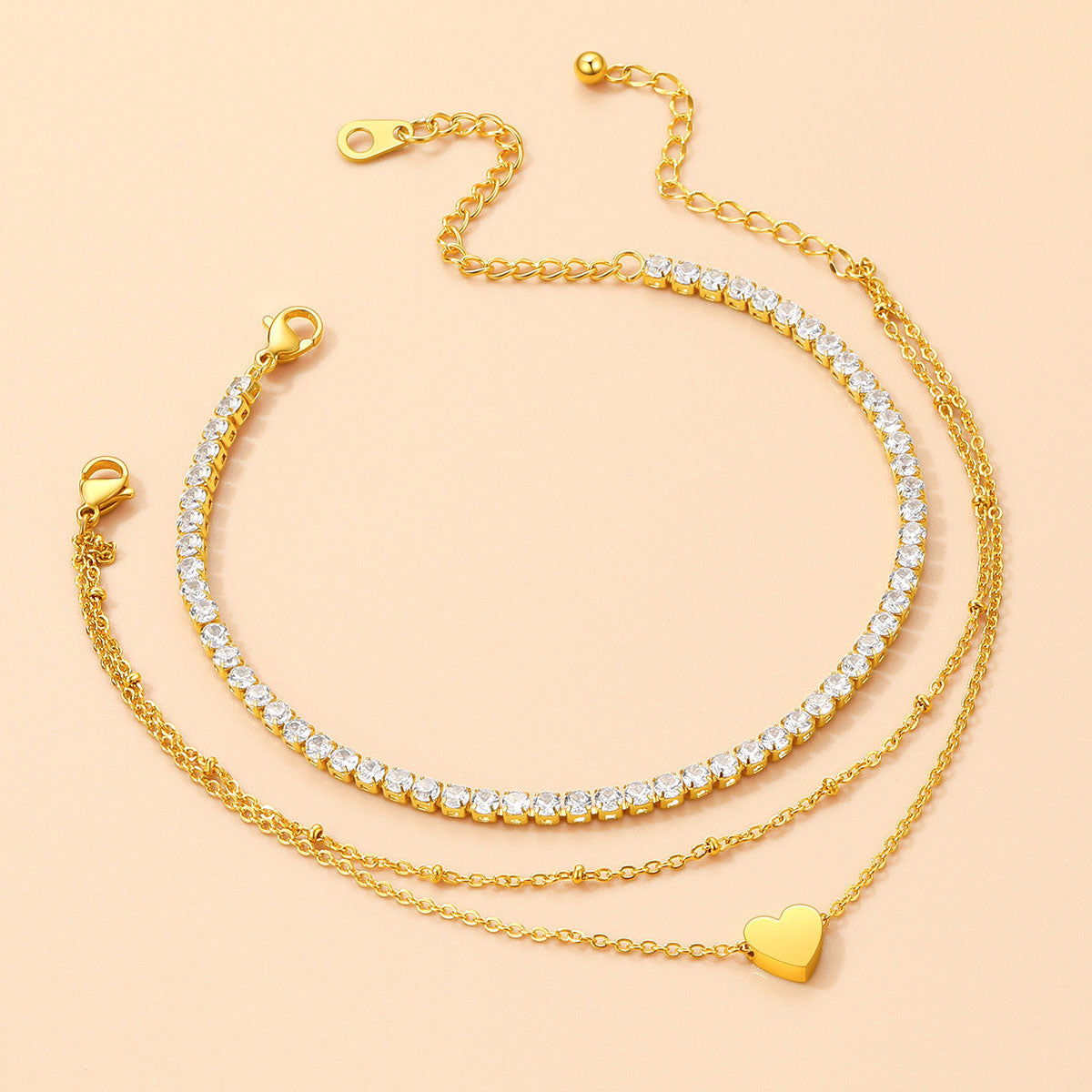 Three gold chain anklet with heart pendants on a beige background
