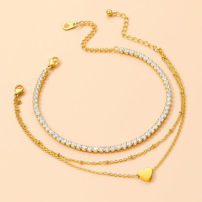 Three gold chain anklet with heart pendants on a beige background