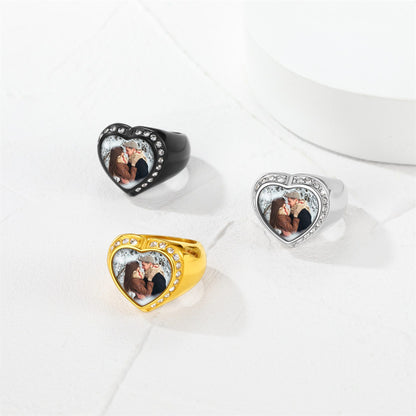 Three heart-shaped picture signet rings in black, gold, and silver on a white surface.