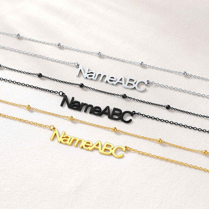 Three layered name necklaces with 'NameABC' on them, in silver, black, and gold, on a white background.