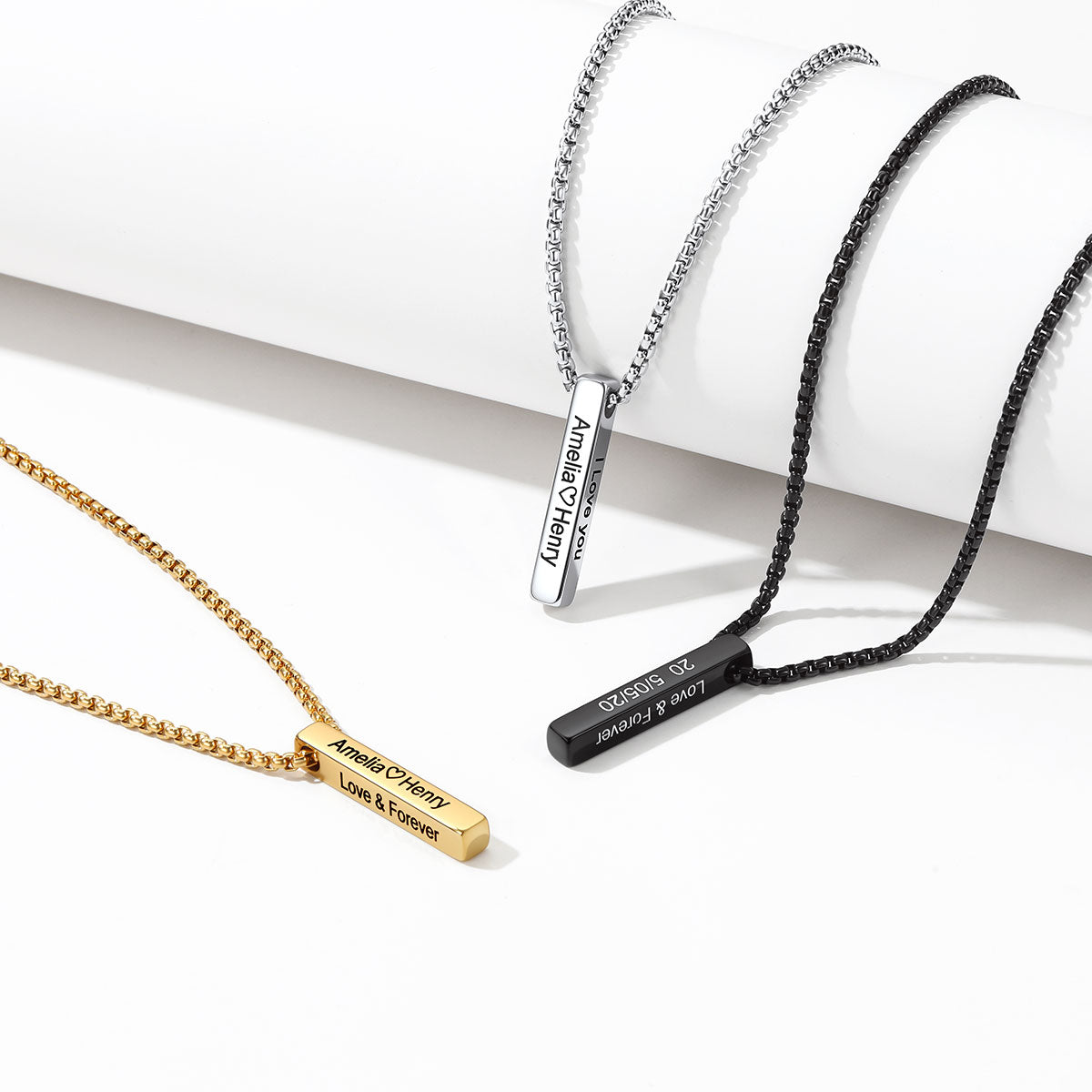 Three personalized engraved bar necklace on chains displayed on a white background. One gold chain necklace with a gold nameplate, one silver chain necklace with a silver nameplate, and one black beaded cord necklace with a black nameplate.