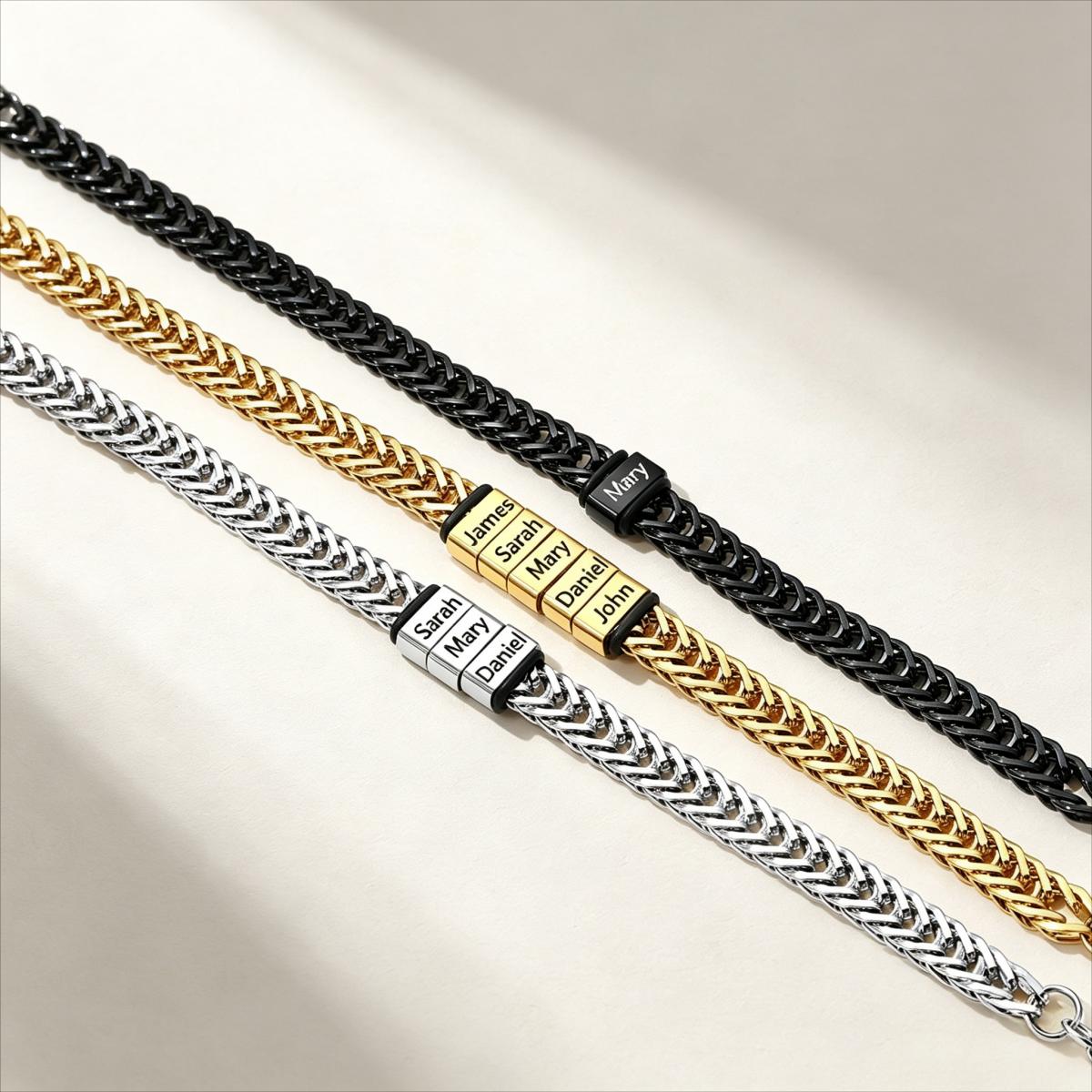 Three personalized name chains arranged diagonally on a light beige background. The top chain is black, the middle chain is gold, and the bottom chain is silver, each featuring a textured cable-style link design with a rectangular nameplate engraved with individual names.